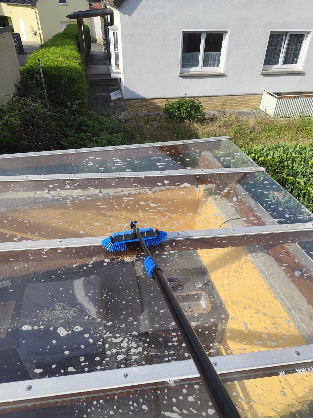 Glasdach einer Terrassenüberdachung wird mit Bürste und Reinigungsmittel gereinigt